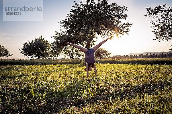 Teenager-Mädchen macht Handstand im grasbewachsenen Feld bei Sonnenuntergang