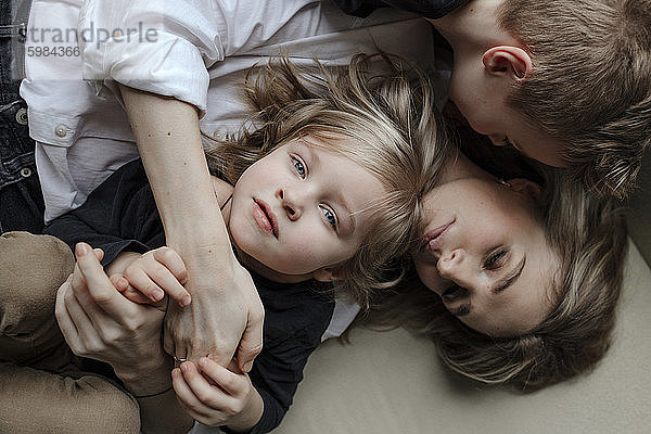 Direktansicht eines blonden Jungen  der mit seinem Bruder und seiner Mutter zu Hause auf dem Sofa liegt