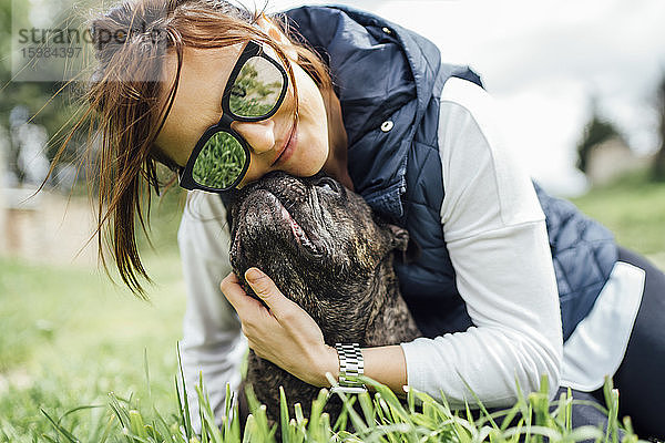 Porträt einer glücklichen Frau  die ihre Bulldogge auf einer Wiese knuddelt