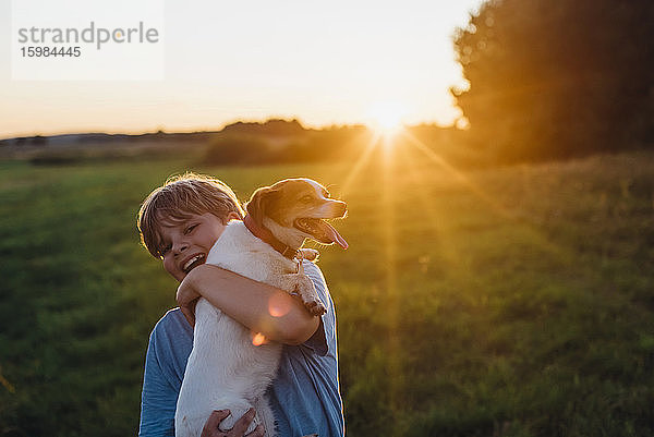 Verspielter Junge mit Hund auf einem Feld bei Sonnenuntergang  Polen