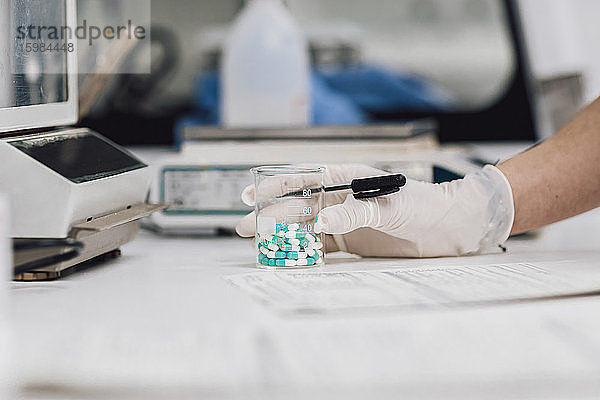 Nahaufnahme einer Technikerin  die einen Becher mit Tabletten auf dem Schreibtisch eines Labors hält