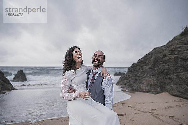 Lachendes Brautpaar am Strand  das seine Frau im Arm hält