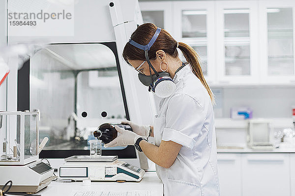Arzt gießt eine Chemikalie in ein Becherglas auf einer Waage  während er im Labor forscht