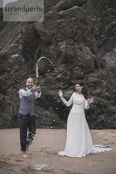 Brautpaar  Mann plantscht mit Champagner am Strand