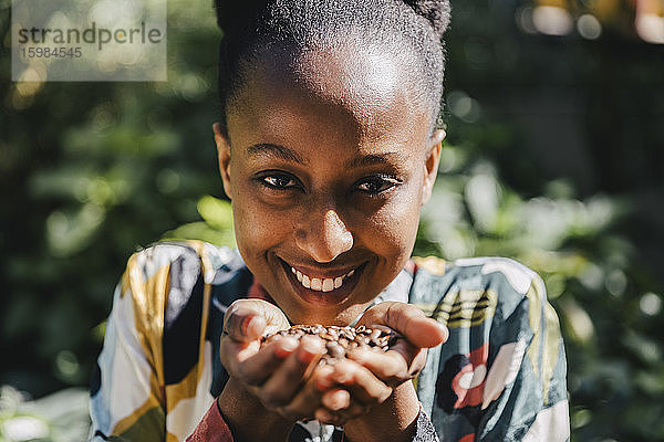 Porträt einer glücklichen jungen Frau  die geröstete Kaffeebohnen in den Händen hält