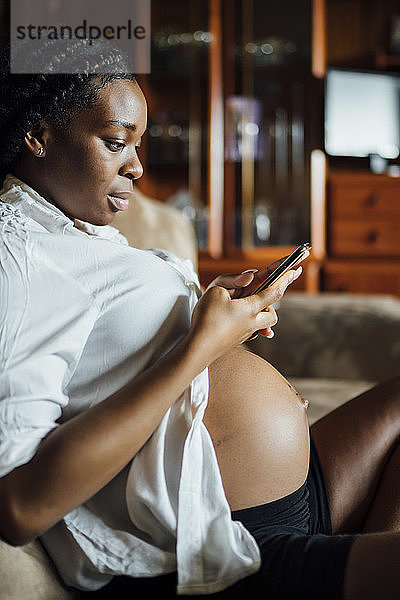 Schwangere junge Frau mit Handy auf der Couch