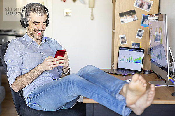 Mann arbeitet von zu Hause aus  macht eine Pause  benutzt Smartphone mit Kopfhörern