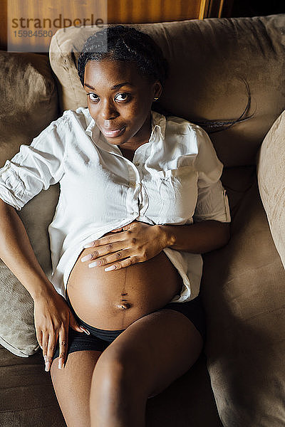 Porträt einer schwangeren jungen Frau auf der Couch