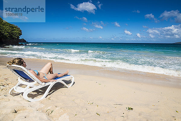 Frau entspannt auf Liegestuhl am Strand gegen blauen Himmel  Grande Anse  Grenada  Karibik