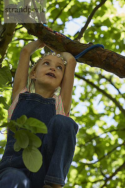 Mädchen mit Gänseblümchenkranz klettert auf einen Baum