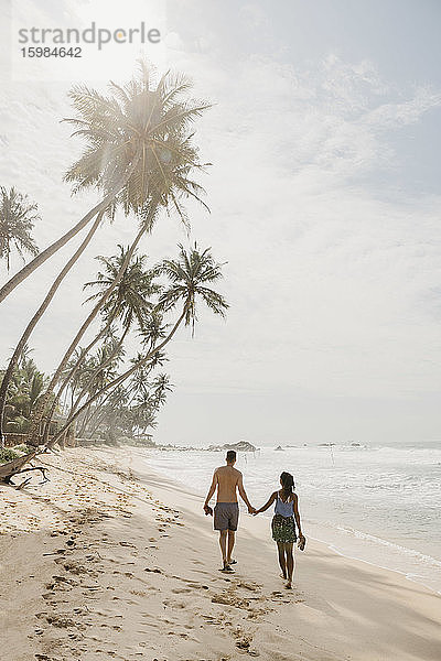Paar in voller Länge am Strand spazierend gegen den Himmel an einem sonnigen Tag  Sri Lanka