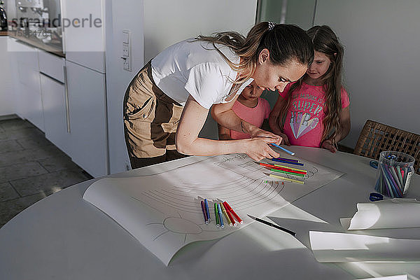 Mutter  die ihren Töchtern beim Zeichnen auf Papier zu Hause hilft