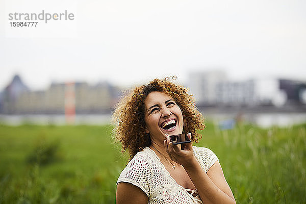 Porträt einer lachenden Frau mit Smartphone im Freien