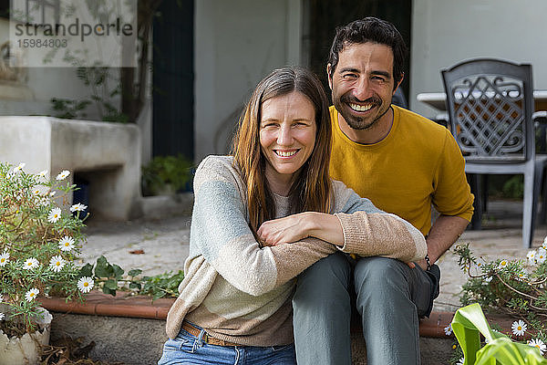 Lächelndes Paar  das auf den Stufen vor dem Bauernhaus sitzt
