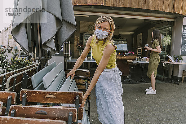 Cafe-Besitzer mit Gesichtsmaske beim Aufstellen von Tischen und Stühlen