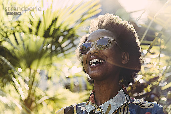 Porträt einer glücklichen jungen Frau mit Sonnenbrille im Garten