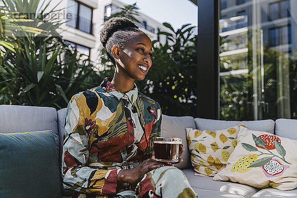 Porträt einer glücklichen jungen Frau  die auf einer Couch im Garten sitzt und schwarzen Kaffee trinkt