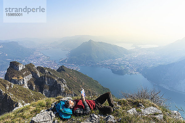 Rückansicht eines Wanderers  der auf einem Berggipfel ein Buch liest  Orobie-Alpen  Lecco  Italien