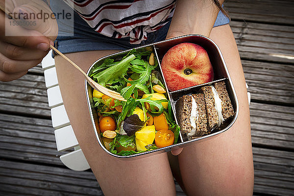 Mittelteil eines Mädchens  das gesund zu Mittag isst  während es auf einer Bank sitzt