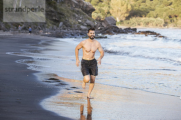 Gut aussehend shirtless Mitte erwachsenen Mann läuft am Strand bei Sonnenuntergang