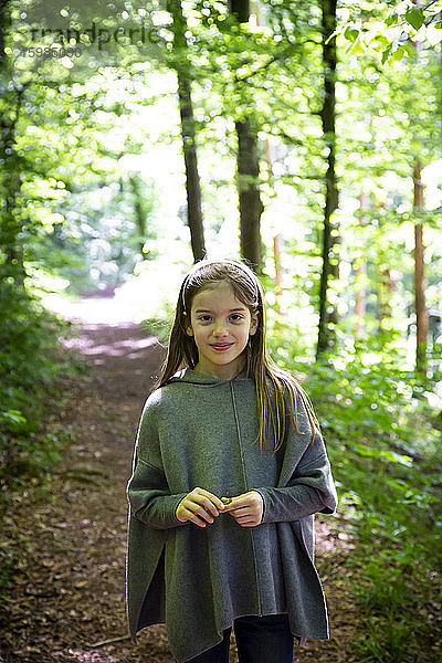 Porträt eines lächelnden Mädchens  das auf einem Wanderweg vor Bäumen im Wald steht