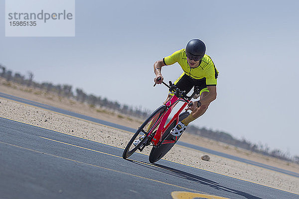 Entschlossener Radfahrer fährt Fahrrad auf der Straße gegen den klaren blauen Himmel in der Wüste in Dubai  Vereinigte Arabische Emirate