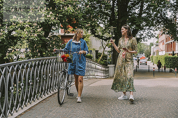 Zwei Frauen mit Fahrrad und Gesichtsmaske gehen auf einer Brücke