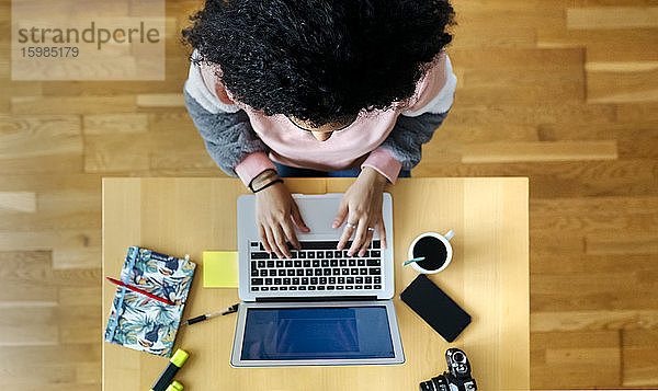 Draufsicht auf eine junge Frau  die von zu Hause aus an einem Laptop arbeitet