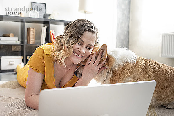 Frau mit Hund benutzt Laptop im Wohnzimmer zu Hause