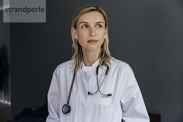 Porträt eines Arztes vor grauem Hintergrund mit Blick in die Ferne