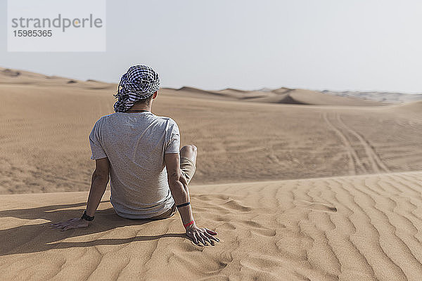 Junger Mann sitzt auf Sanddünen in der Wüste von Dubai  Vereinigte Arabische Emirate