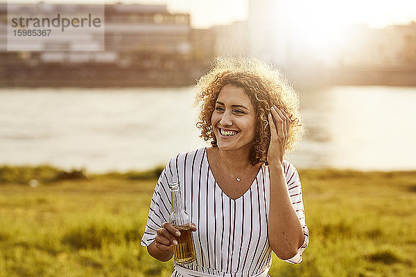 Porträt einer lächelnden Frau mit Glasflasche am Flussufer