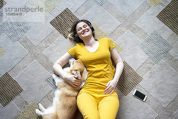 Glückliche Frau mit Kopfhörern  die mit ihrem Hund im heimischen Wohnzimmer kuschelt
