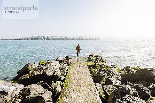 Rückansicht einer Frau in voller Länge  die auf einem Pier steht und auf das Meer blickt  gegen einen klaren Himmel an einem sonnigen Tag