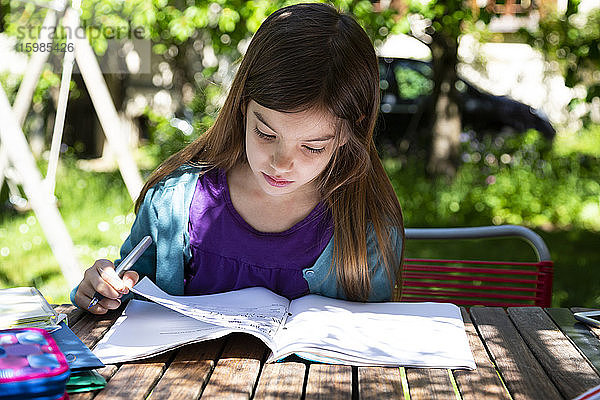 Mädchen sitzt am Gartentisch und macht Hausaufgaben