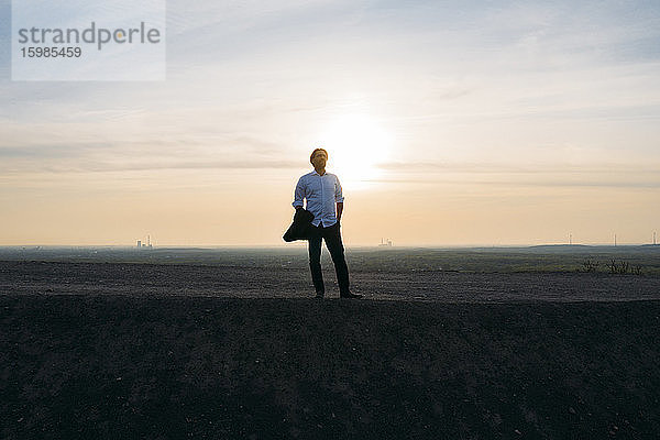 Männlicher Unternehmer steht auf einem Hügel gegen den Himmel bei Sonnenuntergang