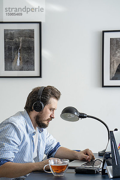 Mann benutzt Laptop und Kopfhörer zu Hause