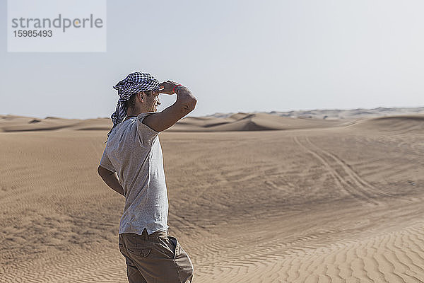 Männlicher Tourist  der seine Augen abschirmt  während er auf Sanddünen in der Wüste von Dubai  Vereinigte Arabische Emirate  steht