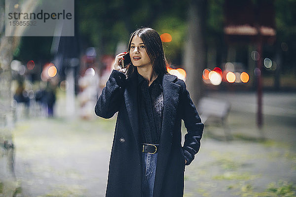 Schöne junge Frau  die mit ihrem Handy spricht  während sie nachts im Freien spazieren geht