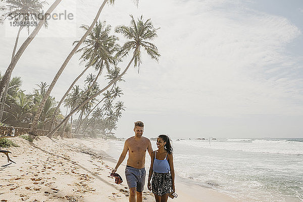 Glückliches Paar  das gemeinsam am Strand spazieren geht  während es seinen Urlaub in Sri Lanka genießt