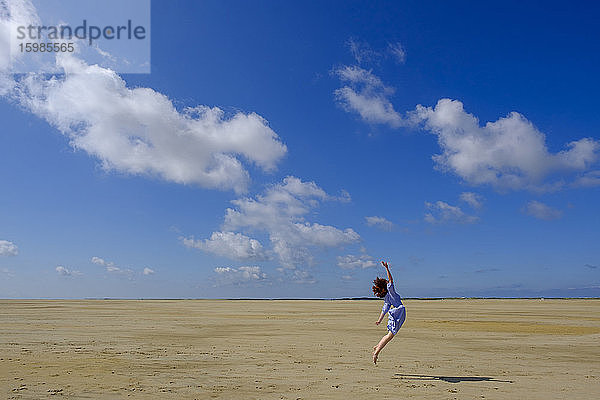 Teenager-Mädchen springt am Strand in voller Länge an einem sonnigen Tag
