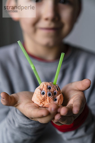 Nahaufnahme eines Jungen  der zu Hause ein Spielzeug-Alien aus Ton und Stroh in der Hand hält