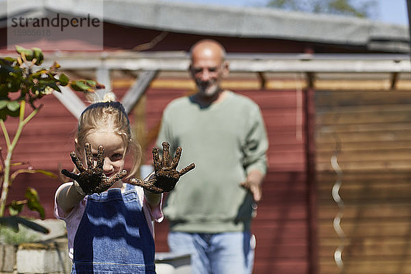 Porträt eines Mädchens mit Großvater im Schrebergarten  das ihre schmutzigen Hände zeigt