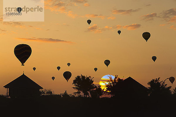Indonesien  Bali  Silhouetten von Heißluftballons fliegen über Küstenhütten bei stimmungsvollem Sonnenuntergang