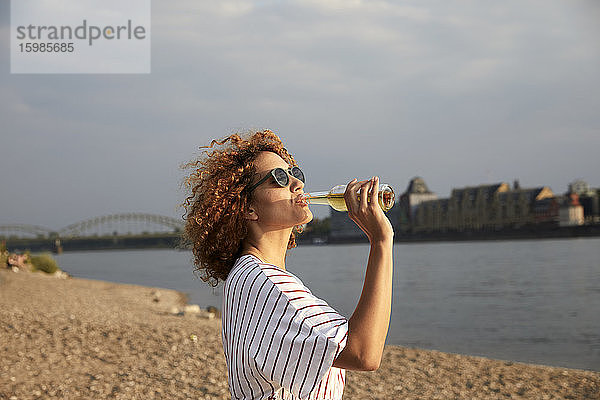 Porträt einer lächelnden Frau mit Glasflasche am Flussufer