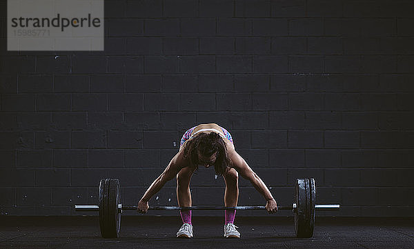 Junge Frau übt Langhantelhocke im Fitnessstudio