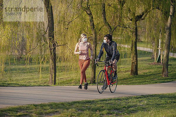 Mann fährt mit dem Fahrrad an einer Frau vorbei  die auf dem Fußweg in einem öffentlichen Park joggt  während COVID-19
