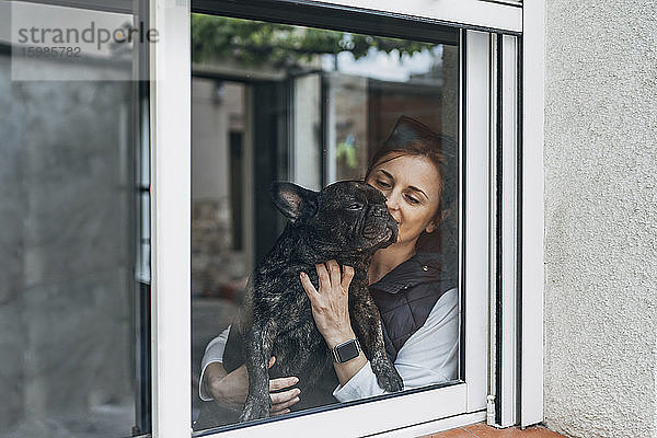 Frau knuddelt ihre Bulldogge hinter dem Fenster