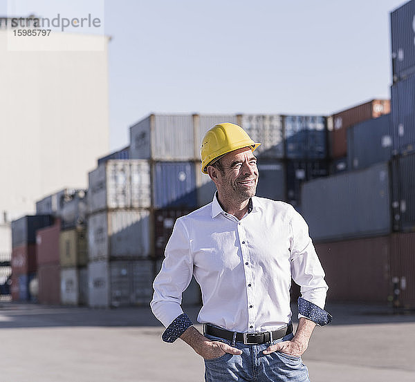 Porträt eines entspannten Geschäftsmannes mit Schutzhelm vor einem Frachtcontainer