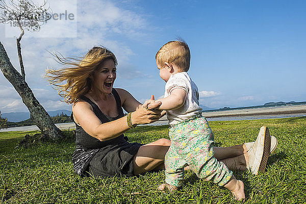 Glückliche Mutter spielt mit ihrer kleinen Tochter auf einer Wiese sitzend  Noumea  Neukaledonien